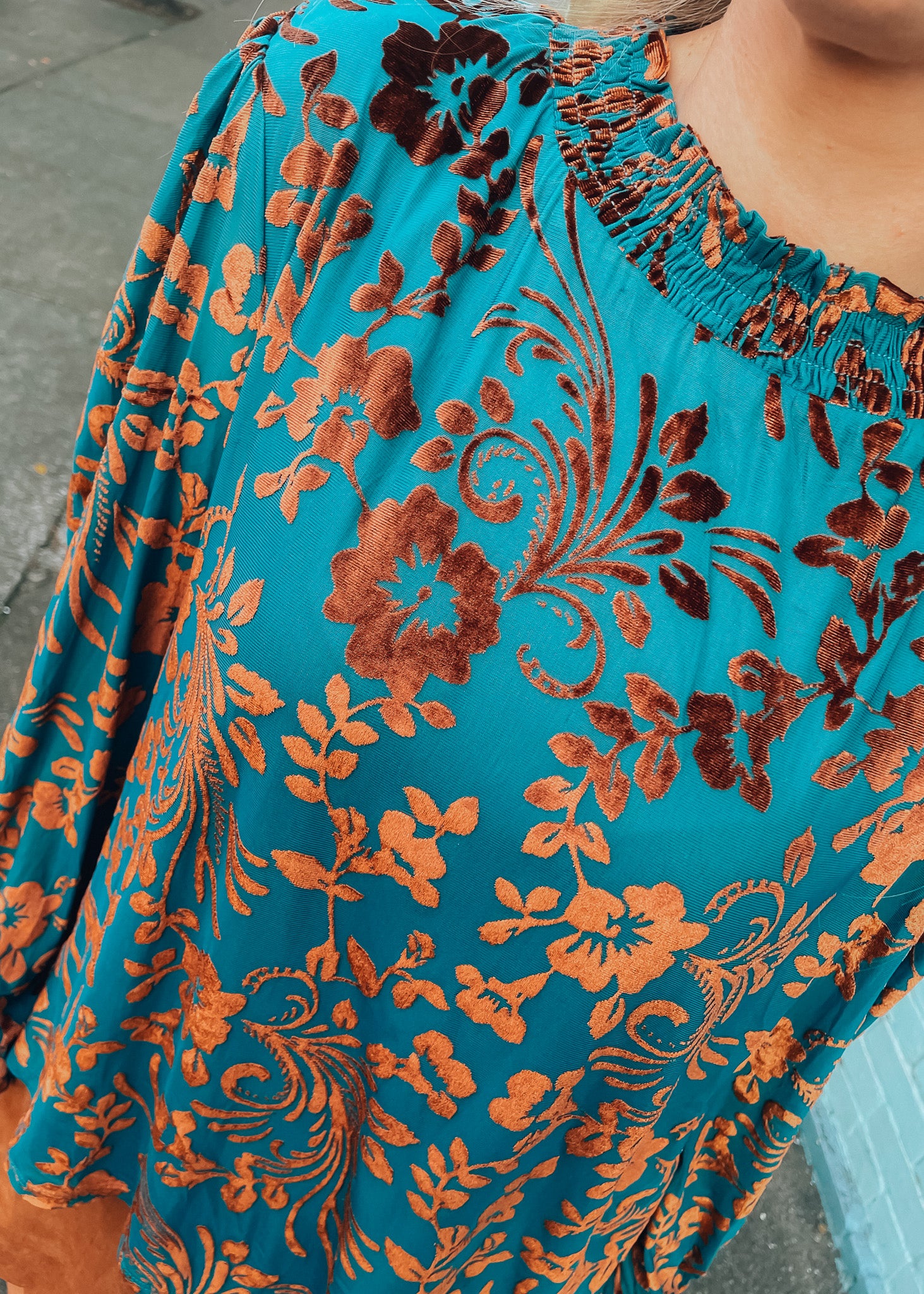 Close-up of a turquoise blouse with orange floral patterns