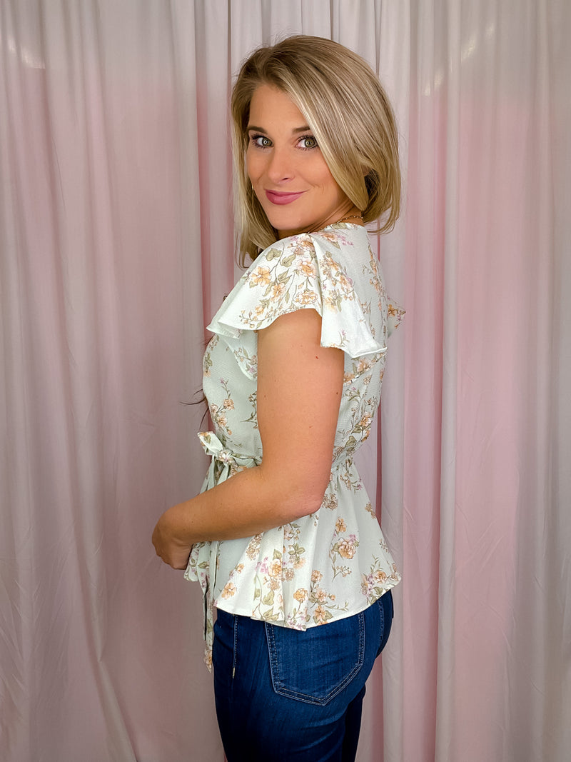 Our Flirty Darling Top showcases a mint base adorned with a beautiful floral print, featuring short sleeves and a V-neck line. The waist is cinched for a flattering fit, and tie detail adds a romantic touch. Make a statement with this elegant and feminine piece.