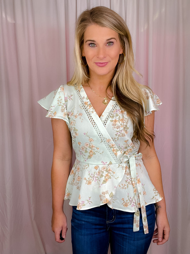 Our Flirty Darling Top showcases a mint base adorned with a beautiful floral print, featuring short sleeves and a V-neck line. The waist is cinched for a flattering fit, and tie detail adds a romantic touch. Make a statement with this elegant and feminine piece.