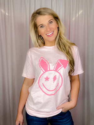 This Smile Face Bunny Tee is the perfect addition to your wardrobe. With its smile face, lighting bolt eyes, bunny ears, short sleeves, and round neck line, this unisex fit shirt will add a cheerful touch to your summer look. Best of all, it's comfortable and cute for the upcoming holiday! -pink