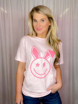 This Smile Face Bunny Tee is the perfect addition to your wardrobe. With its smile face, lighting bolt eyes, bunny ears, short sleeves, and round neck line, this unisex fit shirt will add a cheerful touch to your summer look. Best of all, it's comfortable and cute for the upcoming holiday! -pink