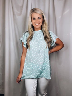 Top features a solid base color, printed detail, ruffled short sleeve. mock detail, airy feel and runs true to size!-MINT