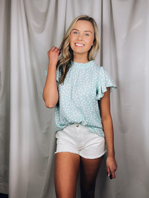 Top features a solid base color, printed detail, ruffled short sleeve. mock detail, airy feel and runs true to size!-MINT