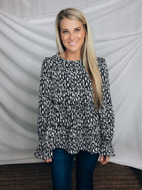 Top features a solid base color, paint stroke design, long sleeves, round neck, light weight material, cinched ruffle sleeves and runs true to size!   100% Polyester -BLACK