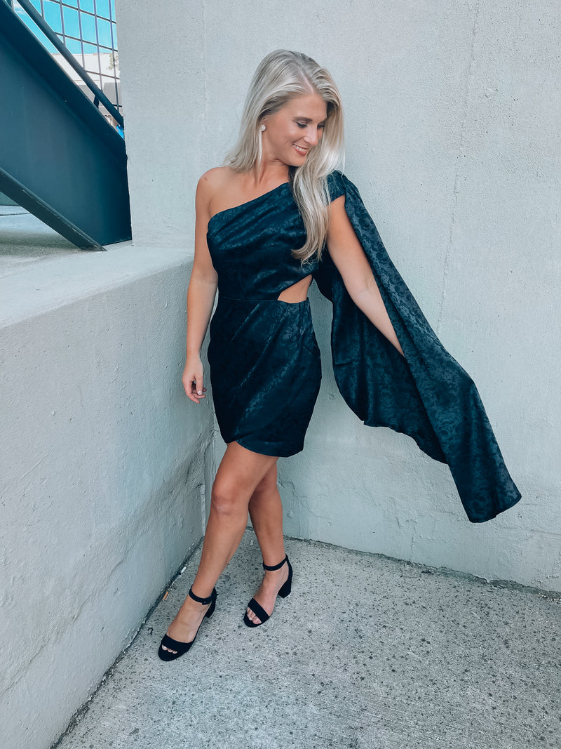 Black satin dress features subtle floral design, side cutout, with a draped, one shoulder detail. Runs true to size!  - Jacquard print - Draped one shoulder - Side ruffle detail - Pleated - Side zipper - 100% Polyester - Lined