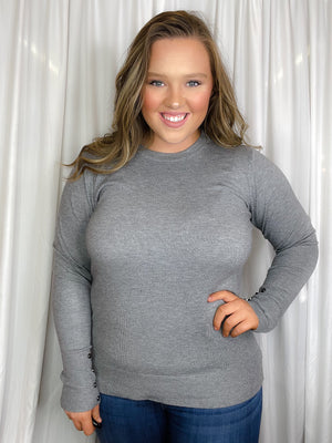 Top features a solid base color, crew neck line, long sleeves, button cuff detailing, soft material and runs true to size! -grey