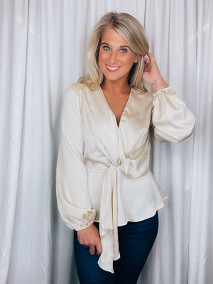 Top features a solid base color, silky material, peplum fit, long sleeves, V-neck line, front draped detail and runs true to size! -champagne