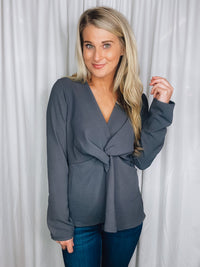 Top features a charcoal base, long sleeves, V-neck line, peplum fit, front knot detail, and runs true to size! 